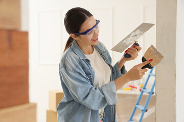 Young woman with putty knives working near wall in room