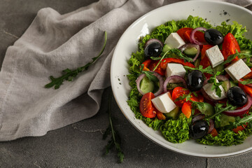 Composition with bowl of tasty Greek salad and napkin on grunge background