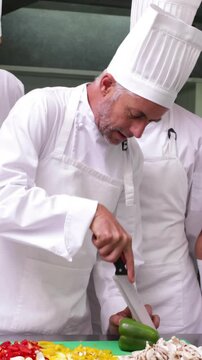 Team of chefs watching head chef slicing vegetables