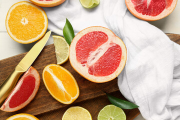 Wooden cutting board, napkin and tasty citrus fruits on white background, closeup