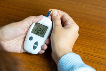Woman's hands checking diabetes and hyperglycemia with digital blood sugar meter. Healthcare and...