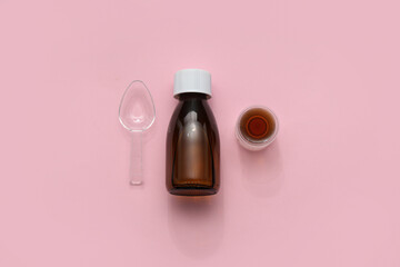 Bottle of cough syrup with measuring cup and spoon on pink background