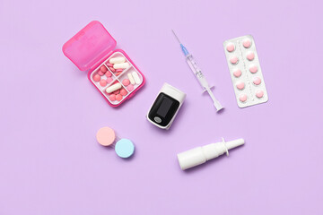 Pulse oximeter, syringe, pill box and container with contact lenses on lilac background