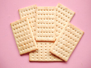 Crackers isolated on pink background. The salty crackers have a crisp, slightly flaky texture with small perforations on the top surface. 