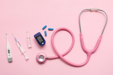 Composition with pulse oximeter, stethoscope, pills, syringe, thermometer and ampule on pink...