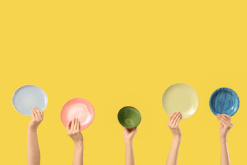 Female hands with bowl and plates on yellow background