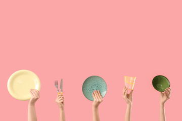 Female hands with plates, bowl, fork, knife and glass on pink background
