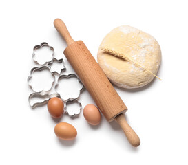 Wooden rolling pin, dough, eggs and cookie cutters isolated on white background