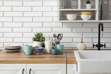 wooden kitchen counter with sink, clean dishes and plants near light brick wall