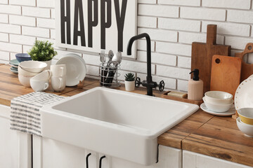 Wooden kitchen counter with ceramic sink, clean dishes and poster hanging on light brick wall