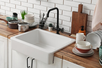 Ceramic sink and clean dishes on wooden counter near light brick wall