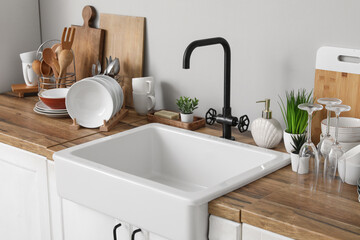 Wooden counter with stylish ceramic sink, clean dishes and kitchen utensils near grey wall