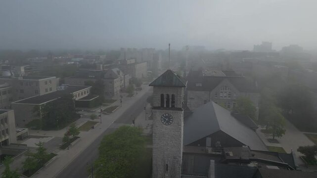 Drone view of the city focusing on an outstanding historical clock tower. The atmosphere is foggy.