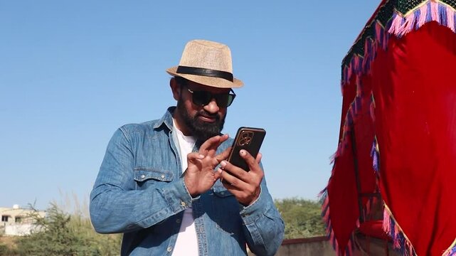 Indian man tourist searching location on smart phone or booking hotel online wearing hat and sunglasses enjoy holiday in rajasthan, Summer vacation, India tourism, 5G network, Wireless Technology.