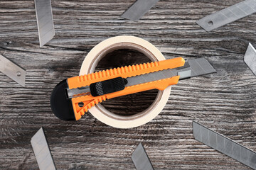 Top view of masking tape and box cutter orange color and many replacement blades on a wooden...