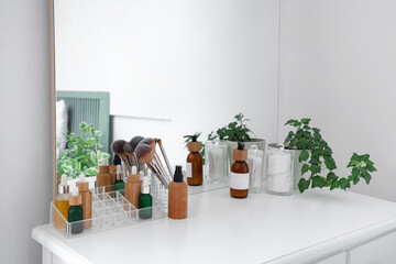 Dressing table with bottles of cosmetic products near white wall in bedroom