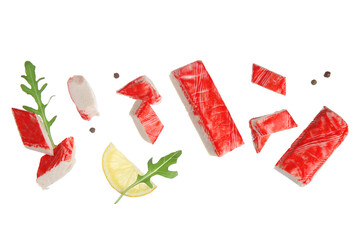 Cut tasty crab sticks with arugula leaves, peppercorns and slice of lemon flying on white background © Pixel-Shot