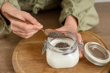 Young woman making chia seed pudding at table in kitchen, closeup