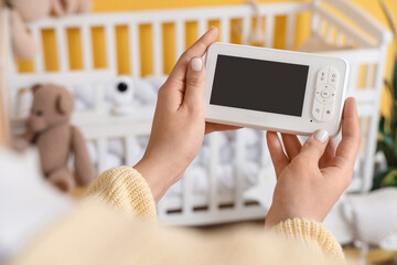 Woman holding baby monitor near crib in children's bedroom, closeup