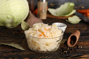 Delicious sauerkraut in bowl with condiments on wooden background. Closeup