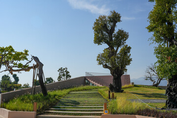 Obraz premium A garden with trimmed trees, green lawn, and trimmed bushes in a background of trees with autumn trees on a foot of a blur mountain from afar under a blue sky 