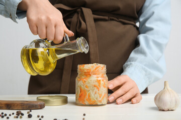 Woman adding oil into jar of sauerkraut in kitchen. Closeup