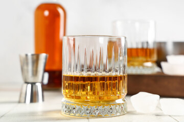 Glass of rum and ice cubes on table against blurred background. Closeup