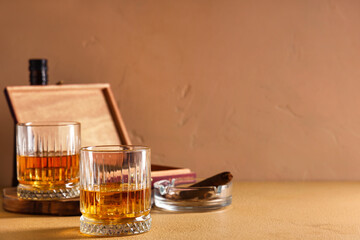 Glasses of cold rum and ashtray with cigar on table against beige background. Closeup