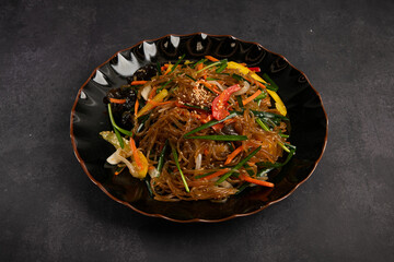 Asian noodles with vegetables and meat in a bowl on a dark background