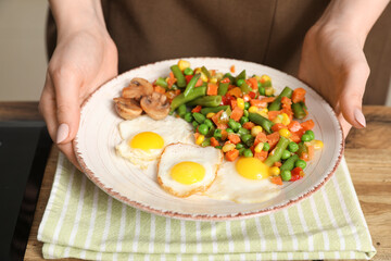 Woman preparing tasty dinner with fried quail eggs and mix of vegetables in kitchen, closeup