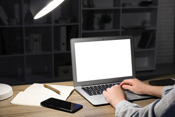 Woman with modern laptop, mobile phone, notebook and pen working at wooden table in evening