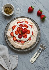 Photo of Pavlova Cake , covered with whipped cream and strawberries, placed on a grey marble table