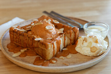 Closeup of Thai Milk Tea Toast with Ice Cream and Almonds. Dessert featuring thick slices of toast topped with Thai tea sauce, ice cream. Garnished with sliced almonds, whipped cream, condensed milk.