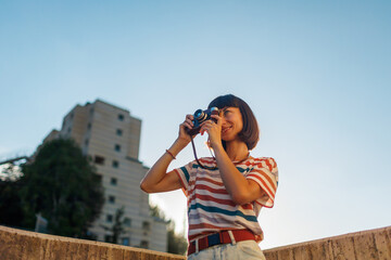 young girl with a camera. Fashionable and attractive beautiful woman with analog film camera takes photos during sunset, .creates content.