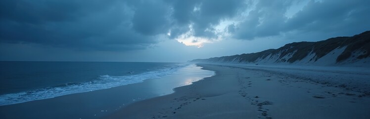 Panoramic shot of Suffolk Coast beach in blue twilight. Clouds over sea at sunset, footprints in sand. Aglow sky, mysterious nature, scenic view, tranquility.
