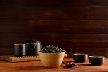 Bowl and spoon with dried green tea leaves on wooden background