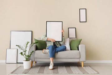 Young woman holding blank photo frame and sitting on sofa in living room