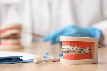 Artificial jaw with toothbrush and clipboard on wooden table, closeup