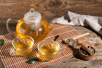 Glass cups of hot green tea and bowl with dried leaves on wooden background