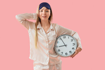 Young woman in pajamas and sleeping mask with clock on pink background