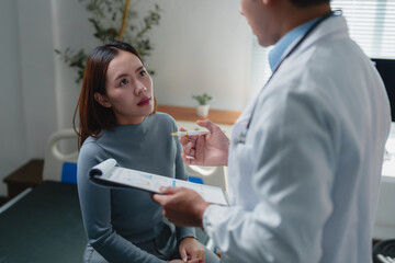 Doctor explaining diagnosis to young female patient holding clipboard and pen, discussing medical...