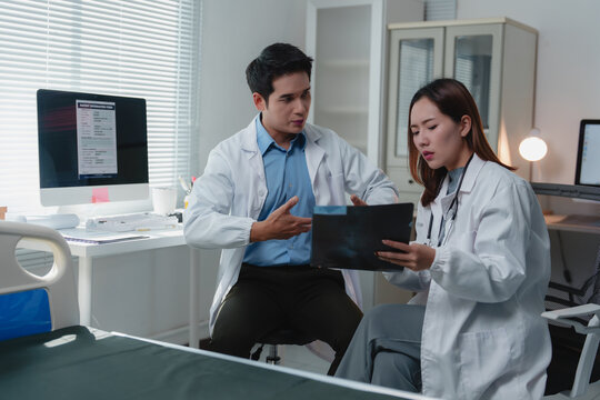 Two doctors examining an x-ray in a hospital room, discussing the diagnosis and collaborating on an effective treatment plan for the patient's health issue - Powered by Adobe
