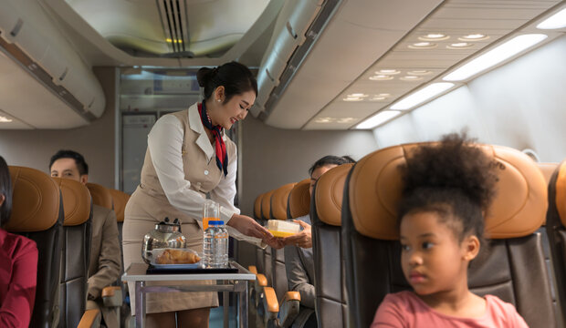 Flight attendant serving food to passenger in airplane cabin. Female air hostess smiling while handing sandwich to businesswoman seated. Airline transportation and travel concept.