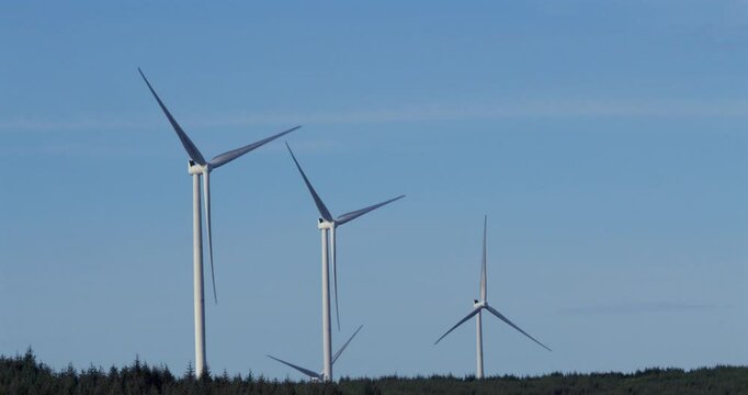 Wide shot of wind turbines rotating with blue sky on the A A4061 at Hendre'r Mynydd Car Park,