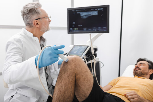 Ultrasound examination of knee. Experienced ultrasound doctor examines knee of athletic man after injury
