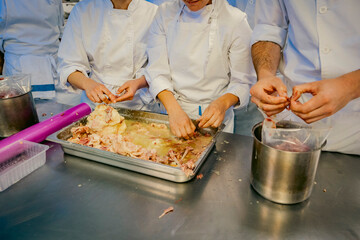 Group of chefs in white uniforms preparing and processing raw meat in a professional kitchen. Hands-on culinary training focused on food preparation and hygiene standards.