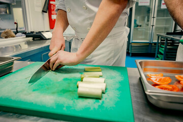 Close-up of a chef cutting fresh vegetables on a green cutting board in a professional kitchen. Precision knife skills are essential in culinary training and food preparation.