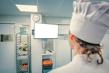 Professional chef in a clean commercial kitchen using a computer for recipe management or kitchen operations. Modern technology in the culinary industry.