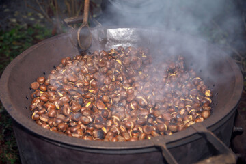 Roasted chestnuts smoking in large metal pan for outdoor winter snack preparation