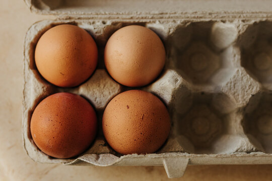 Overhead shot of four brown eggs in mostly empty egg carton